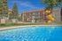 Vibrant apartment complex featuring a sparkling swimming pool, colorful playground, and inviting lounge chairs under a clear blue sky.