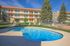 Inviting apartment pool area with sun loungers, surrounded by a well-maintained building and lush greenery, under a clear blue sky.