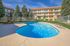 Inviting apartment complex with a sparkling outdoor pool, surrounded by lush greenery and ample lounge seating, perfect for relaxation under clear blue skies.