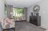 Chic living room with vibrant patterned chairs, sleek modern console with mirror, and large bright window offering a lush garden view.
