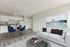 Modern open-concept living space featuring a cozy white sofa, elegant art piece, and a chic dining area with blue chairs, seamlessly connected to a sleek kitchen.