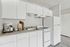 Bright, modern kitchen with sleek white cabinetry, a spacious countertop featuring an espresso machine, and a classic stove and fridge combo.