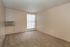 Bright and airy room with fresh beige walls, plush carpet, and natural light from a large window with vertical blinds, featuring efficient wall-mounted air conditioning.