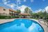 Inviting apartment complex pool area with vibrant blue skies, lush greenery, and relaxing lounge chairs.