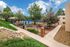 Charming apartment courtyard with lush greenery, a sparkling pool, and inviting outdoor dining areas under blue umbrellas.