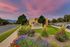 Charming view of The Hills Apartments entrance with vibrant gardens and a breathtaking sunset sky.