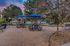 Charming outdoor patio area featuring picnic tables with blue umbrellas, a grill, and serene surroundings overlooking a sparkling pool.