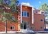 Charming apartment building with an inviting entrance, surrounded by lush pine trees and bathed in warm sunlight.