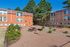 Charming apartment exterior with vibrant terracotta walls, lush greenery, and inviting outdoor seating area under clear blue skies.