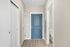 Inviting apartment hallway featuring a chic blue front door, elegant hardwood flooring, and bright, crisp walls.