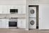 Modern kitchen with white cabinetry and stainless steel appliances, featuring a sleek oven and microwave beside an in-unit stacked washer and dryer.
