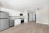Bright and modern kitchen with sleek white cabinets, stainless steel appliances, and wood-look flooring, leading into a spacious open-concept living area.