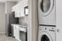 Modern kitchen and in-unit laundry featuring sleek white cabinetry, stainless steel appliances, and stacked washer-dryer for convenient living.