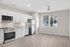 Chic modern apartment kitchen with sleek white cabinetry, stainless steel appliances, and bright natural light from large windows showcasing a scenic view.