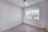 Bright bedroom with modern ceiling fan, large window with vertical blinds offering scenic views, and sleek wood flooring.