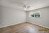 Bright and inviting bedroom with sleek wooden flooring, large window, and a modern ceiling fan, perfect for relaxation.