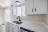 Bright and modern kitchen with sleek white cabinets, double sink, and ample natural light streaming through large windows.