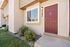 Inviting entrance of a modern apartment with a maroon door, lush greenery, and a charming exterior.