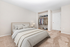 Bright and inviting bedroom with plush carpeting, neatly organized open closet, and a comfortable bed dressed in soothing neutral tones.