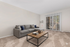 Modern living room with plush carpeting, cozy gray sofa, decorative pillows, and a rustic wood coffee table near sliding glass doors offering abundant natural light.