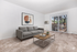Bright and inviting living room with modern gray sofa, artistic wall decor, and a view of the lush outdoors through sliding glass doors.