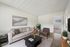 Inviting living room with a comfortable beige sofa, modern chair, and chic decor, featuring a black coffee table, cozy rug, and vibrant flower arrangement.
