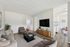 Contemporary living room with cozy seating and sleek TV setup, opening to a bright kitchen area.