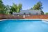 Inviting apartment complex pool surrounded by lush greenery and a charming brick wall under a clear blue sky.