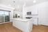 Bright and modern kitchen with sleek white cabinetry, stainless steel appliances, and large island countertop, featuring natural light from sliding glass doors leading to a balcony.