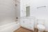 Modern bathroom featuring sleek white cabinetry, elegant fixtures, and a refined tiled shower area with a cozy bathtub for relaxation.