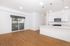 Modern open-concept kitchen and living area with sleek wooden floors, stainless steel appliances, and abundant natural light from large patio doors.