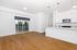 Bright and modern open-concept living space featuring sleek hardwood floors, an elegant kitchen with island, and large sliding glass doors leading to a balcony with scenic views.
