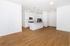 Modern open kitchen with sleek white cabinetry, stainless steel appliances, and elegant lighting, set against rich wooden floors.