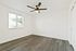 Bright bedroom with elegant gray wood flooring, a modern ceiling fan, and a large window offering natural light.