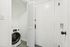 Compact laundry area featuring a modern front-load washer with sleek white walls and folding doors.