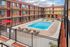 Inviting apartment complex courtyard featuring a sparkling pool, lounge chairs, and vibrant red accents under a blue sky.