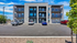 Modern three-story apartment building with private balconies and ample parking space, set against a bright blue sky.