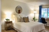 Cozy bedroom with stylish decor, featuring soft lighting, a comfortable bed with decorative pillows, and a bright window with blue curtains.
