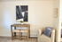 Cozy apartment corner featuring a stylish armchair with a plush blue pillow, a rustic wooden table with stools, and modern abstract wall art.