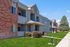 Charming two-story apartment building with brick and stucco exterior, surrounded by lush green landscaping and a clear blue sky.
