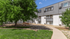 Inviting apartment exterior with lush green surroundings, modern architecture, and a well-maintained walkway under a clear blue sky.