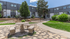 Charming apartment complex with lush greenery, a stone pathway, and a quaint outdoor seating area.