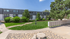 Charming apartment exterior with lush green landscaping and convenient mailbox area under a clear blue sky.
