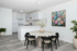 Bright and elegant kitchen and dining area with modern white cabinetry, marble round table, and cozy black chairs. Accented with vibrant floral artwork and lush green plants, offering a serene and welcoming atmosphere.