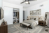 Elegant bedroom featuring a plush bed with neutral bedding, spacious walk-in closet, stylish wooden furniture, and a large decorative mirror.