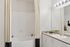 Elegant bathroom featuring a sleek white bathtub with a stylish curtain, modern countertop, and a large mirror with contemporary lighting.