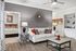 Chic apartment living room showcasing elegant decor with a cozy white couch, vibrant orange cushions, stylish wall art, and modern ceiling fan, adjacent to a charming bedroom.