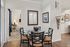 Charming dining area with glass table and stylish chairs, adorned with modern artwork and cozy accents, leading into a well-lit bedroom.