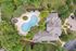 Aerial view of a luxurious apartment complex with a beautifully landscaped courtyard and uniquely shaped pool, surrounded by lush greenery and ample lounge seating.