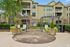 Charming apartment complex facade with elegant stonework, lush greenery, and inviting outdoor seating area under stylish pergolas.